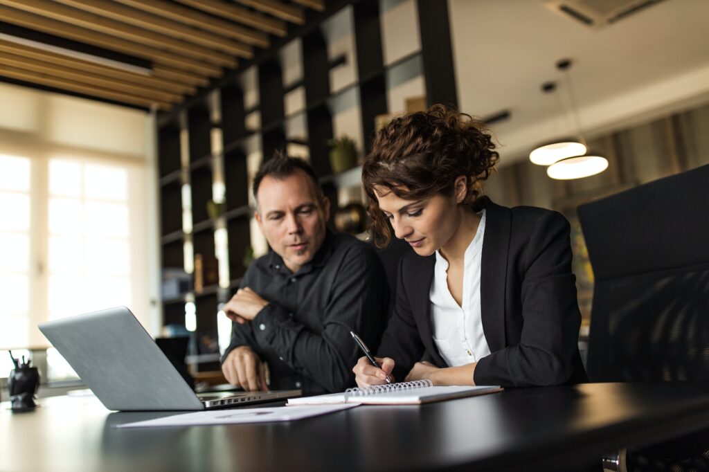 Businesswoman taking notes while businessman talks, portrait.