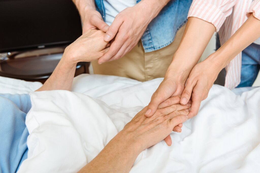 partial view of young people hands holding hands of elderly woman lying on hospital bed
